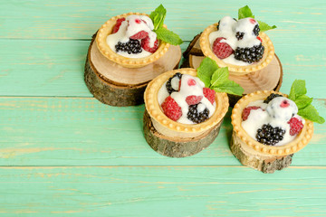 Tartlets with berries and cream, leaves of mint on decorative stumps.