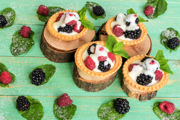 Tartlets with berries and cream, leaves of mint, sprinkled with sugar,  on decorative stumps. And also a pattern of leaves and berries around.