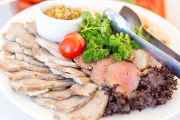 Meat plate with delicious pieces of sliced ham, sausage, meat, tomatoes, parskey with herbs and spoon. Close up with selective focus.