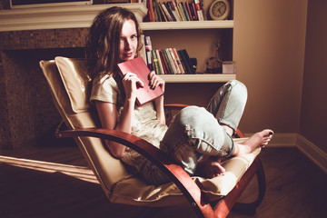 Enjoying time at home. Pretty woman holding paper old book with anticipation in comfortable modern chair. Natural light. Cozy home. Bright sunny day. Knowledge and learning concept. Bookworm student