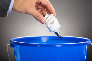 Hand Throwing Energy Efficient Light Bulb In Blue Bucket