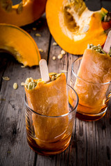 Ideas for autumn dishes from pumpkins. Treats for a Thanksgiving party, Halloween. Pumpkin ice cream popsicles with seeds, in glasses with maple syrup. On wooden old rustic table. Copy space