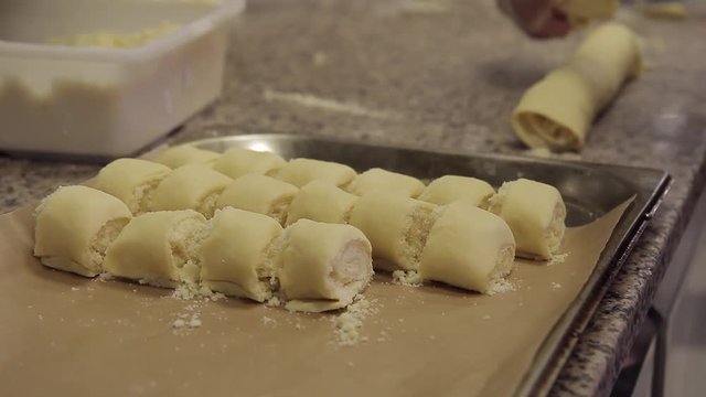 Cook cooks sweet cheesecakes and piles it on dish before baking indoor. cuts small slice of dough with dairy product and folds in rows to pan covered paper. Chef prepares for large number of guests in