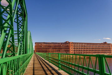 Green metal bridge over river with nineteenth century brick mill buildings in background © Heidi Besen