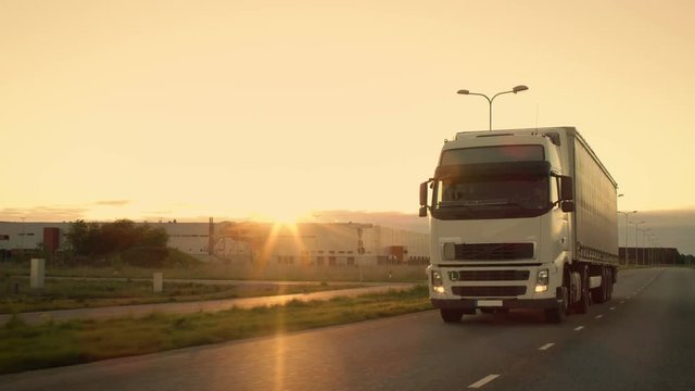 Front-View Camera Follows Semi-Truck with Cargo Trailer Driving on a Highway. He's Speeding Through Industrial Warehouse Area with Sunset in the Background. Shot on RED EPIC-W 8K Helium Cinema Camera.