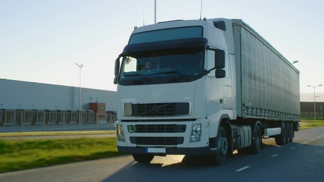 Semi Truck with Cargo Trailer Moving on a Highway. White Truck Drives Through Industrial Warehouse Area. Shot on RED EPIC-W 8K Helium Cinema Camera.