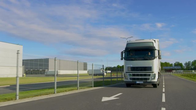 Two White Trucks with Cargo Semi Trailers Driving Out of Industrial Loading Area
