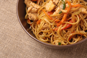 Stir fried noodle with chicken and vegetables in brown plate with chop sticks. Chinese cuisine. Closeup.