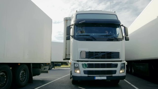 Frontal View of White Semi Truck with Cargo Trailer Drives into Parking Place and Parks with Other Vehicles. Shot on RED EPIC-W 8K Helium Cinema Camera.
