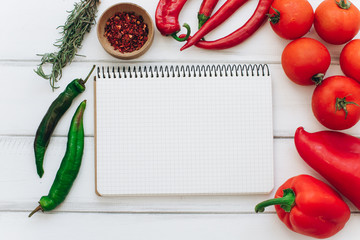 Notebook with a recipe. Red pepper, rosemary, tomatoes and green chilies on a white wooden background.