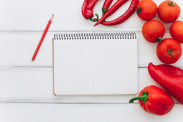 Notebook with recipe. Red pepper, tomatoes and chilies on a white wooden background.
