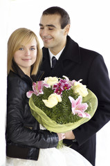 Portrait of beautiful Smiling bride holding bouquet while happy groom standing in background over white/Romantic newlywed couple standing head to head on white background