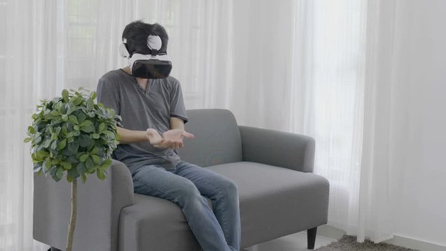 4K : Excited Asian young man wearing virtual reality goggles at home