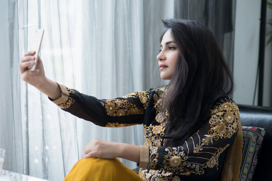 Muslim woman in yellow dress taking selfie.