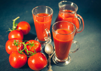 Red tomatoes and juice on dark background. Tomato juice. Selective focus. Low-key lighting