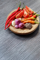Ingredients of hot and spicy sambal placed on wooden plate at black wooden table and some space for your text