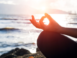 Yoga concept. Closeup woman hand practicing lotus pose on the beach at sunset
