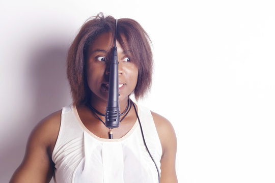 Young african woman singing holding a microphone, cheerful and funny, indoors, over a white background.