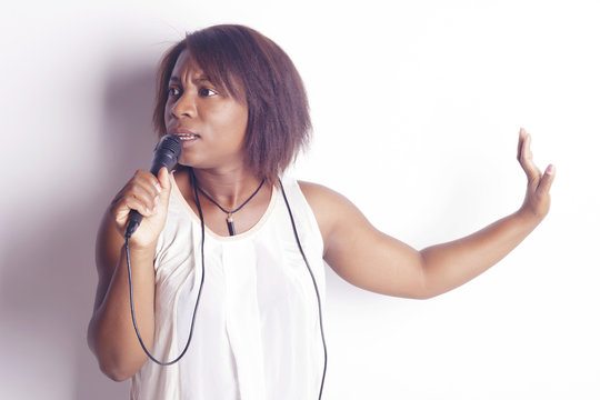 Young african woman singing holding a microphone, cheerful and funny, indoors, over a white background.