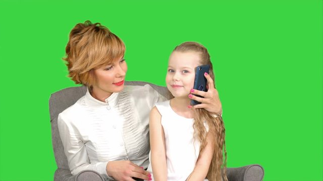 Little daughter having phone call, sitting near her mother on a Green Screen, Chroma Key