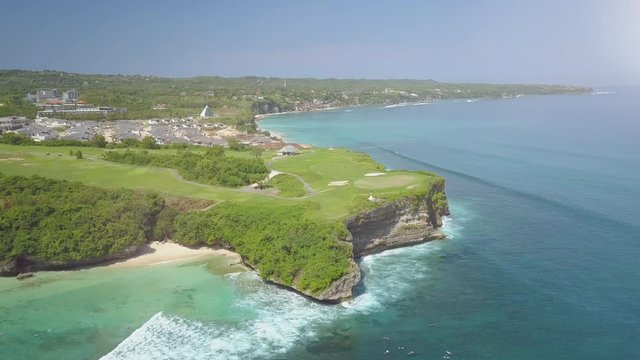 Aerial, lens flare flying above luxury bungalow tourist resort and new kuta golf course at the rim of the rocky and cliffy coastline overlooking vast blue ocean