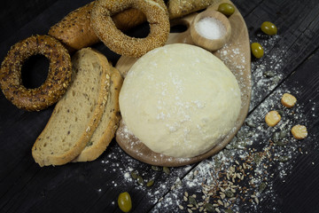 Dough on a wooden board with snacks set and olives in the background