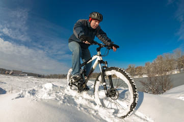 Obraz premium Man enjoys his ride on a bicycle in a deep snow, next to the river