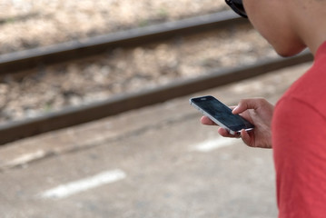 A man wearing a red shirt is using a cell phone while waiting for a train at the train station.