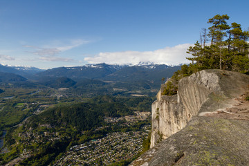 View point from cliff above valley with mountains and clouds.