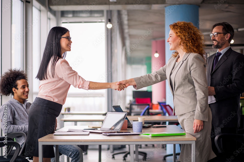 Wall mural working space. two businesswomen shaking hands. deal between two business teams.