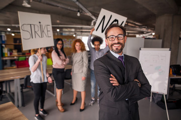 Fototapeta premium Modern office concept, director standing with his back to striking cowokers. unhappy employees holding posters with words strike and no.