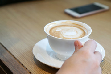 Hot Mocha - Closeup hand holding a cup of coffee with milk and latte art on wooden table, Morning Breakfast.