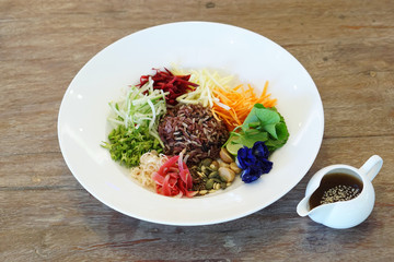 Spicy Rice Salad with variety of vegetables (carrot, winged bean, cucumber, gotu kola, beetroot, torch ginger, butterfly pea, lemon grass, macadamia, flaxseed) served with budu dressing, Thai food.
