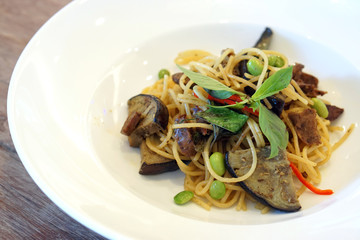Closeup a white plate of Green Curry Spaghetti with grilled purple eggplant (aubergine), roasted pleurotus eryngii mushroom and edamame bean decorated with basil, Vegan or vegetarian Food concept.