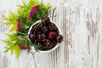 A tasty cherry in a little bowl with flowers and herbs.