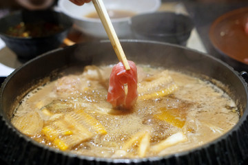 Hand holding raw pork using chopsticks on hot pot with smoke for Japanese hot pot also known as Shabu Shabu or Sukiyaki is Japanese style.