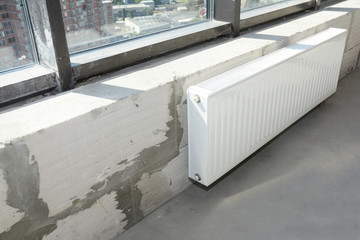 Installing metal white radiator heating with thermostat in new house construction.