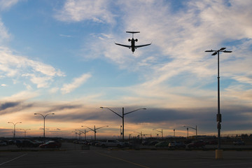 Fototapeta na wymiar Plane flying low over parking lot while sunset
