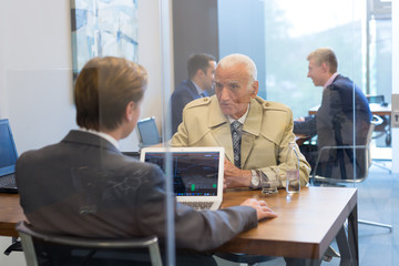 Young financial advisor sitting in front of laptop, consulting senior client with his investment strategy. Business people on business meetings.