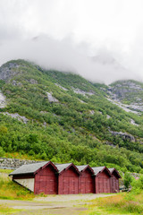 Fototapeta na wymiar Five red wooden boathouses with dramatic mountainside behind. Rainclouds over the mountain. Location Eidfjord in Norway.
