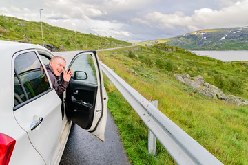 Happy passenger smiling and waving to camera from open door on small car in mountainous landscape. Location Hardangervidda in Norway.
