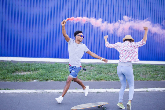 young couple jumping and dancing with pink smoke bomb, hipster having fun on the streets 