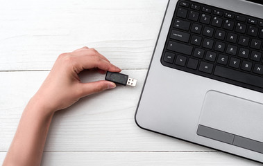 Hand inserting USB flash drive into laptop computer on white background. Close up of woman hand...