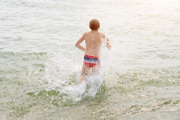 Boy jumping in sea waves. Jump with water splashes. Summer vacation, sunny day, ocean coast. Toned image.