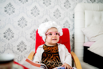 Funny baby costumed like a granny sitting in the chair.