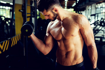 Young attractive bodybuilder is working out with dumbbells.