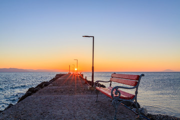 Fototapeta na wymiar Empty red bench at seashore during sunrise.