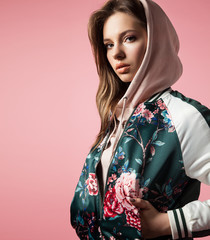 Portrait of a stylish girl in a bomb jacket with floral print standing on a pink background