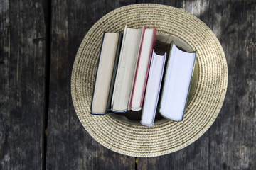 A stack of books in a straw hat of a canoe on a wooden village table