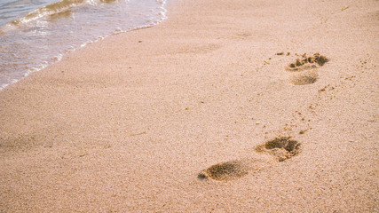 Wave and footprints on clear sandy beach.
